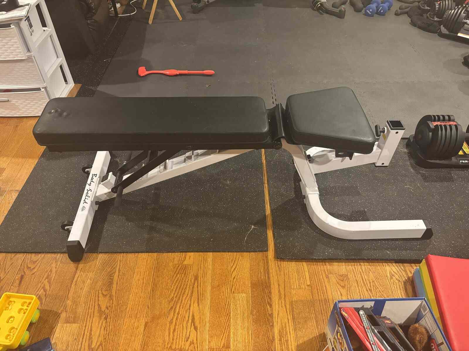 Body-Solid white FID bench on rubber mats with FitRx adjustable dumbbell in the background