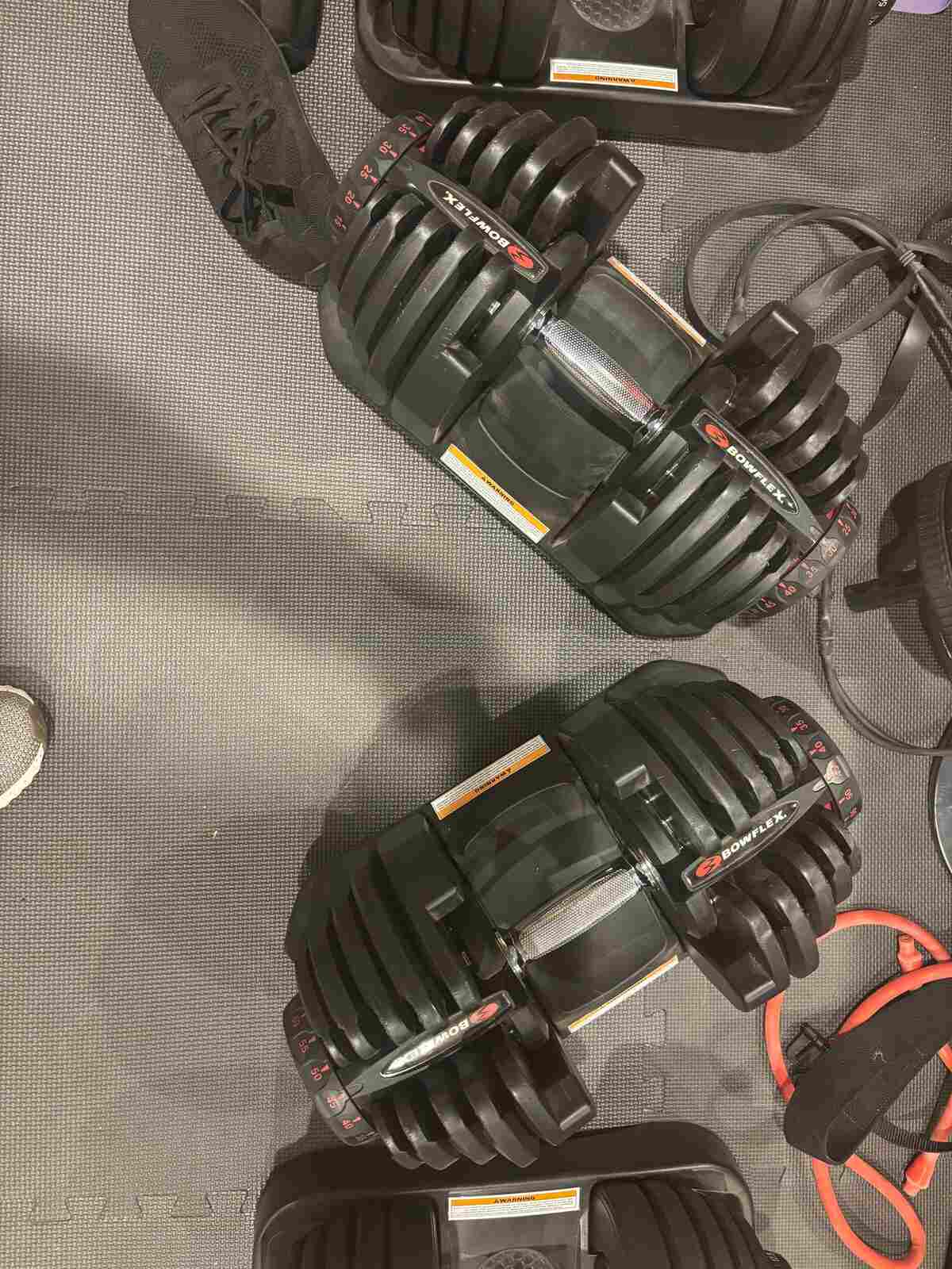 Bowflex SelectTech 552 and 1090 adjustable dumbbells in cradles on foam mats in a personal home gym