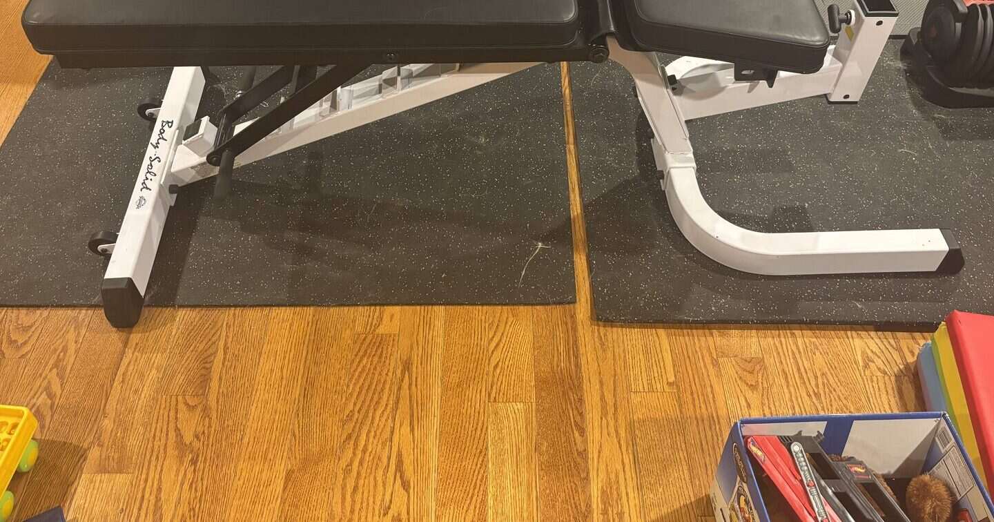 Black rubber gym mats under a Body-Solid bench on a home gym floor — site owner’s owned gear